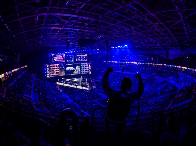MOSCOW, RUSSIA - 14th SEPTEMBER 2019: esports video games event. Happy dedicated electronic sports fan cheering for his favorite team on a tribunes in front of a big screen with hand raised.