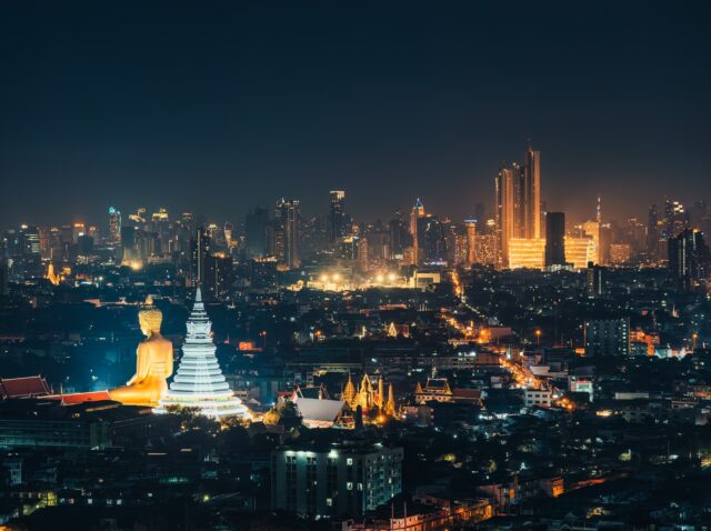 Cityscape of Bangkok night scene with building exterior, buddha in temple and department store glowing in crowded downtown at Thailand