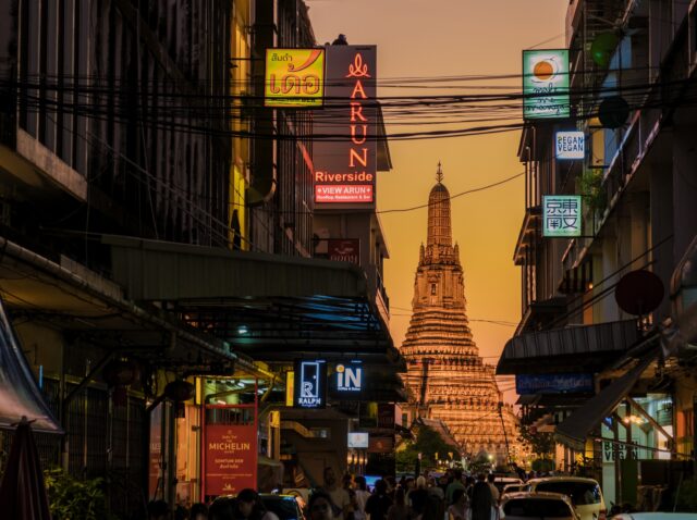 Bangkok Thailand 10 January 2025, As the sun sets, the stunning silhouette of Wat Arun towers above the bustling streets of Bangkok. Colorful signs light up the evening, creating a lively atmosphere